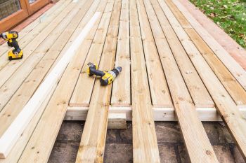 Partially installed wooden deck boards with cordless drills on a backyard deck frame